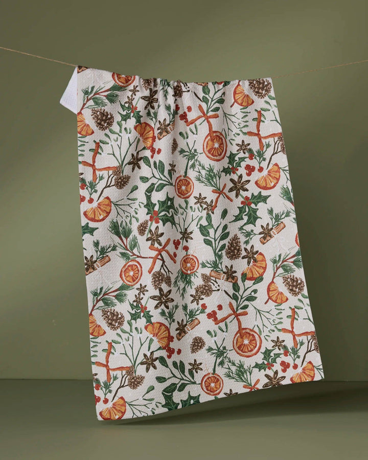 Geometry Canela Tea Towel featuring citrus slices, cinnamon sticks, pinecones and winter greenery