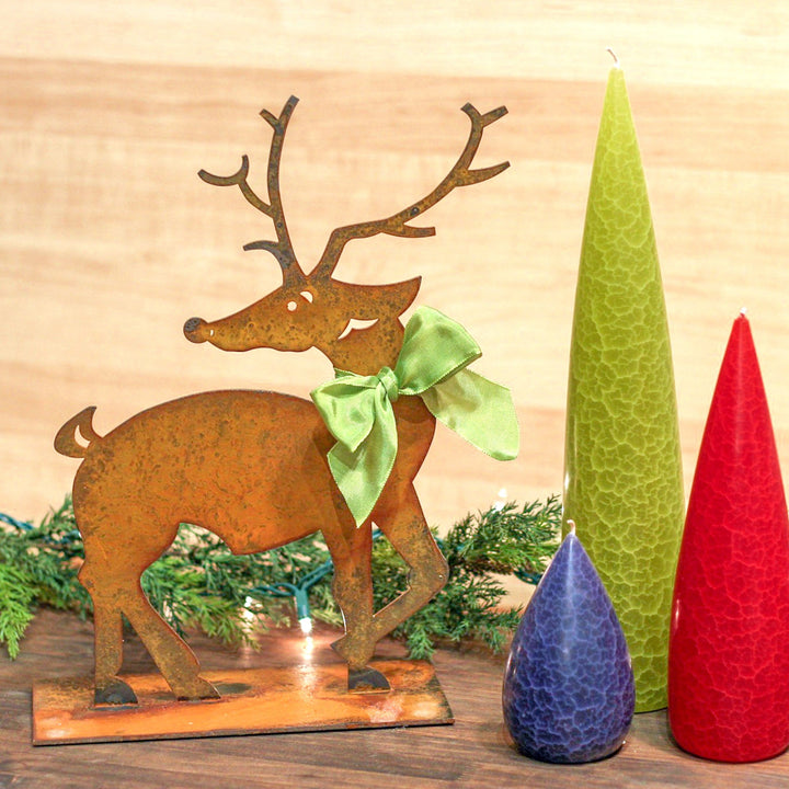 Prairie Dance Dancer rusted steel reindeer with green bow beside colorful candles